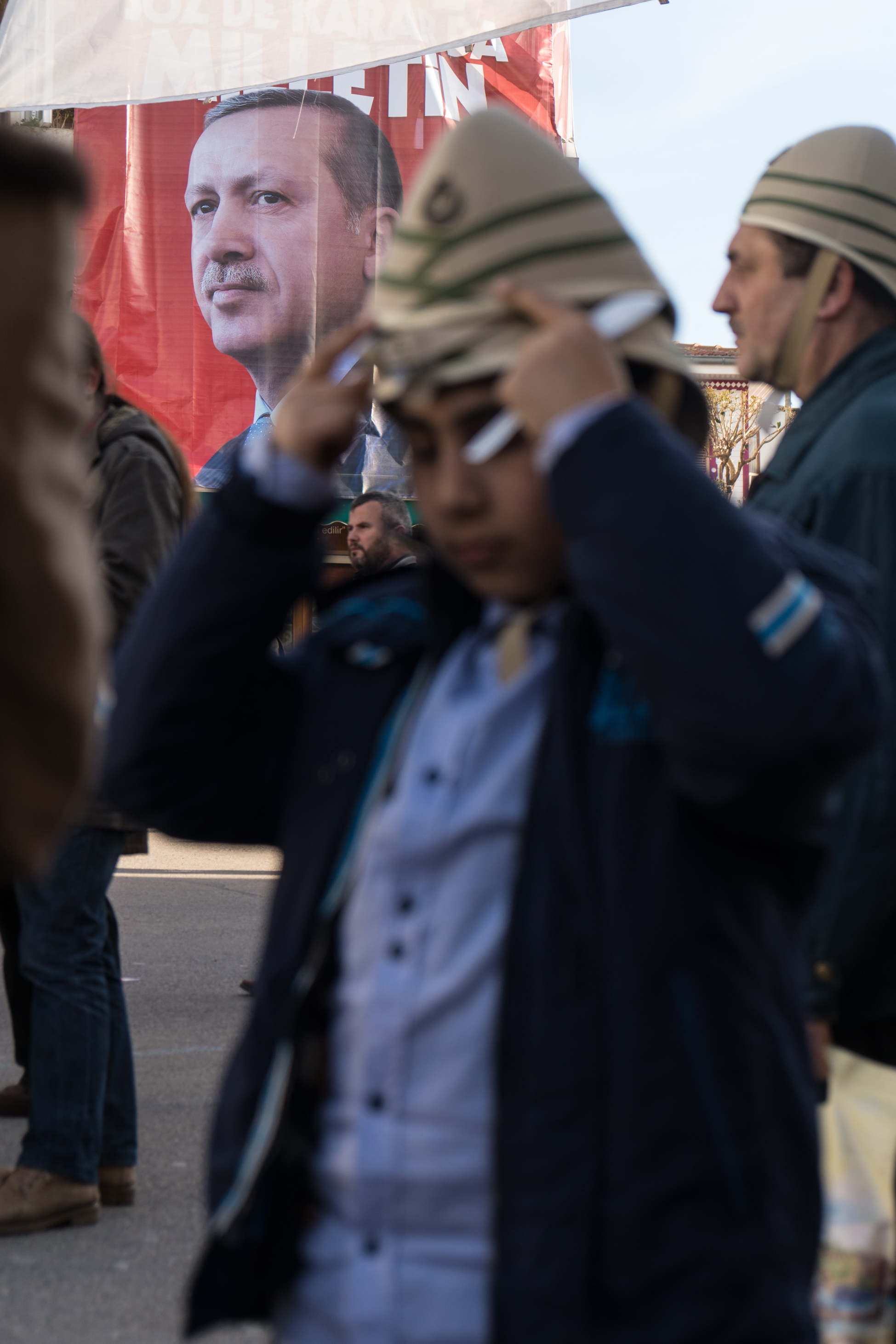 In Istanbul, in Eminönü, a pro-Erdogan rally falls on Remembrance Day for Ottomans who fell in WWI. Ralliers chant “yes” for a referendum that would allow the presidential leader full control of the government, eradicating parliament. A boy dons a Turkish Sun Helmet against an Erdogan flag.