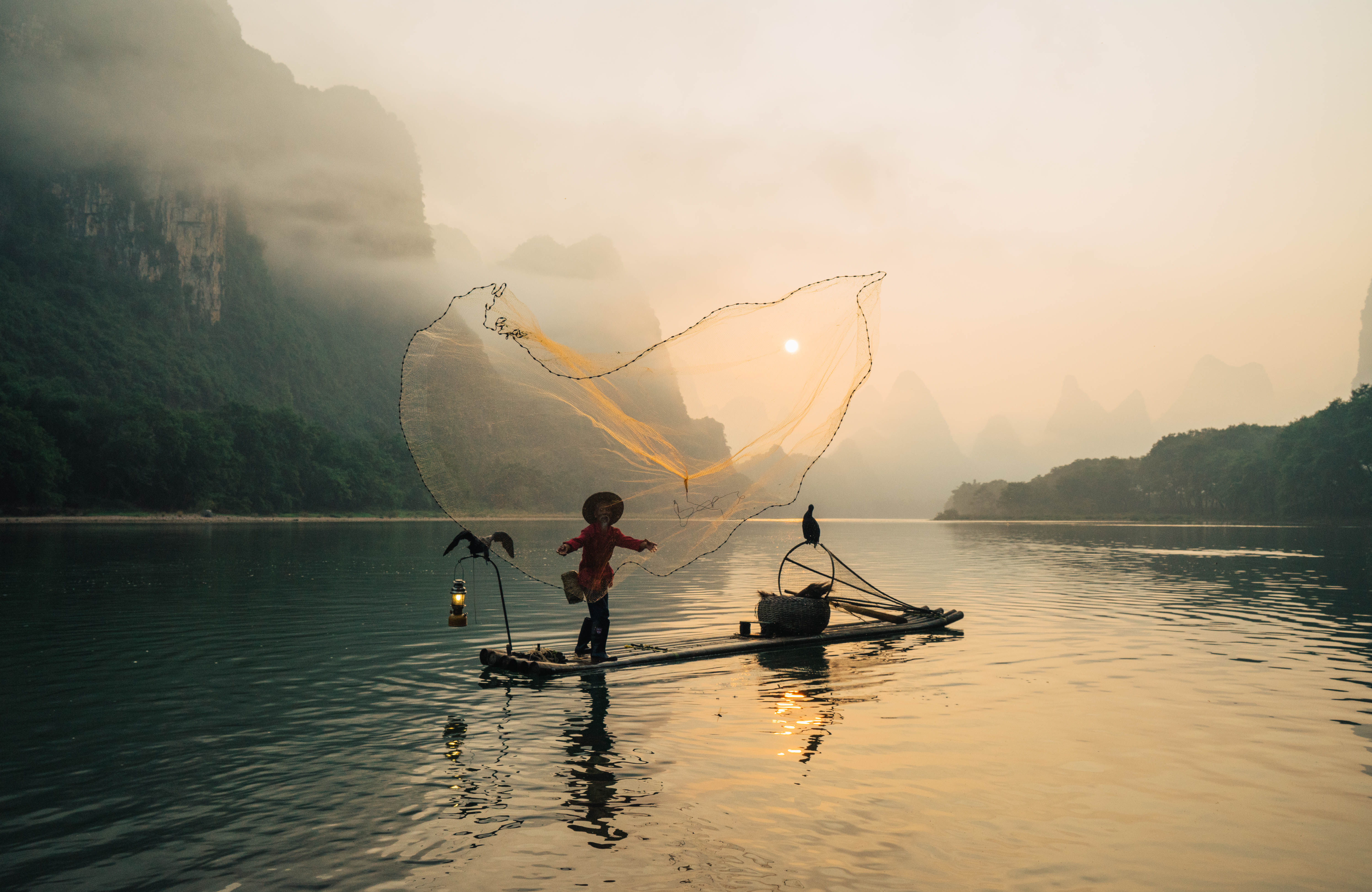 Casting a net into the Li River as the sun rises behind the karst mountains. 
