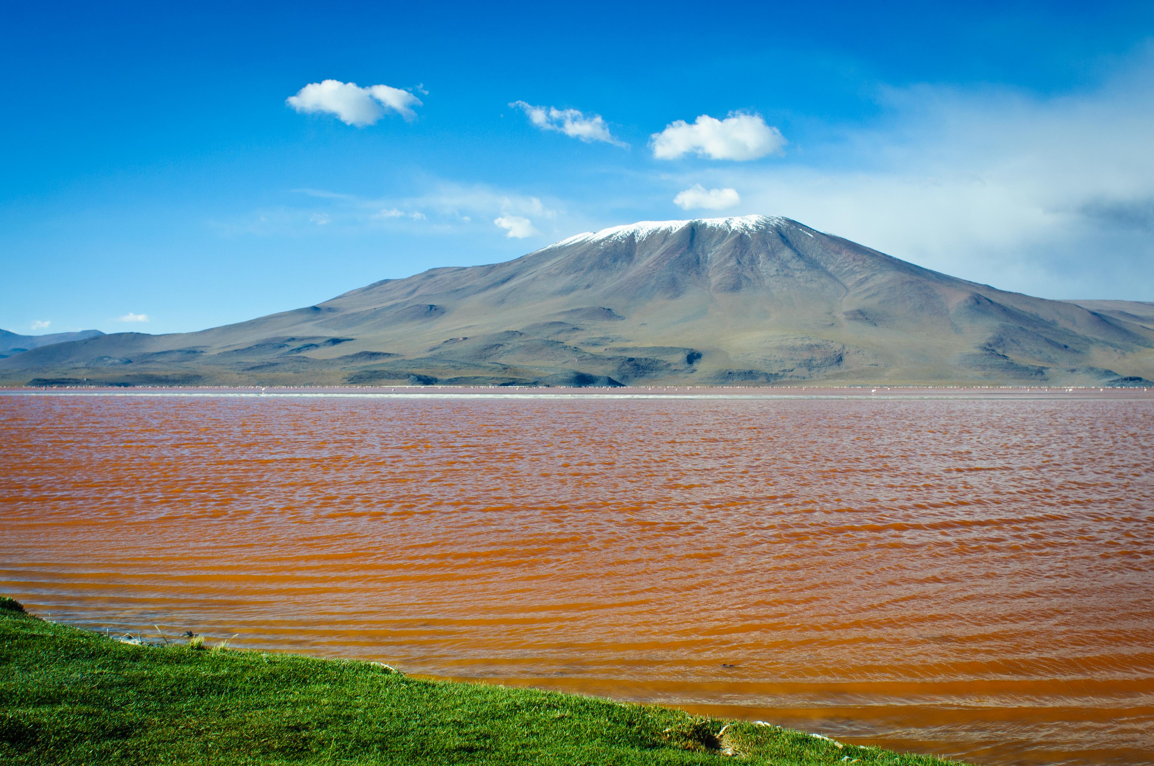 A large ochre mineral lake, surrounded by a narrow green perimeter. In the distance an ancient volcano.