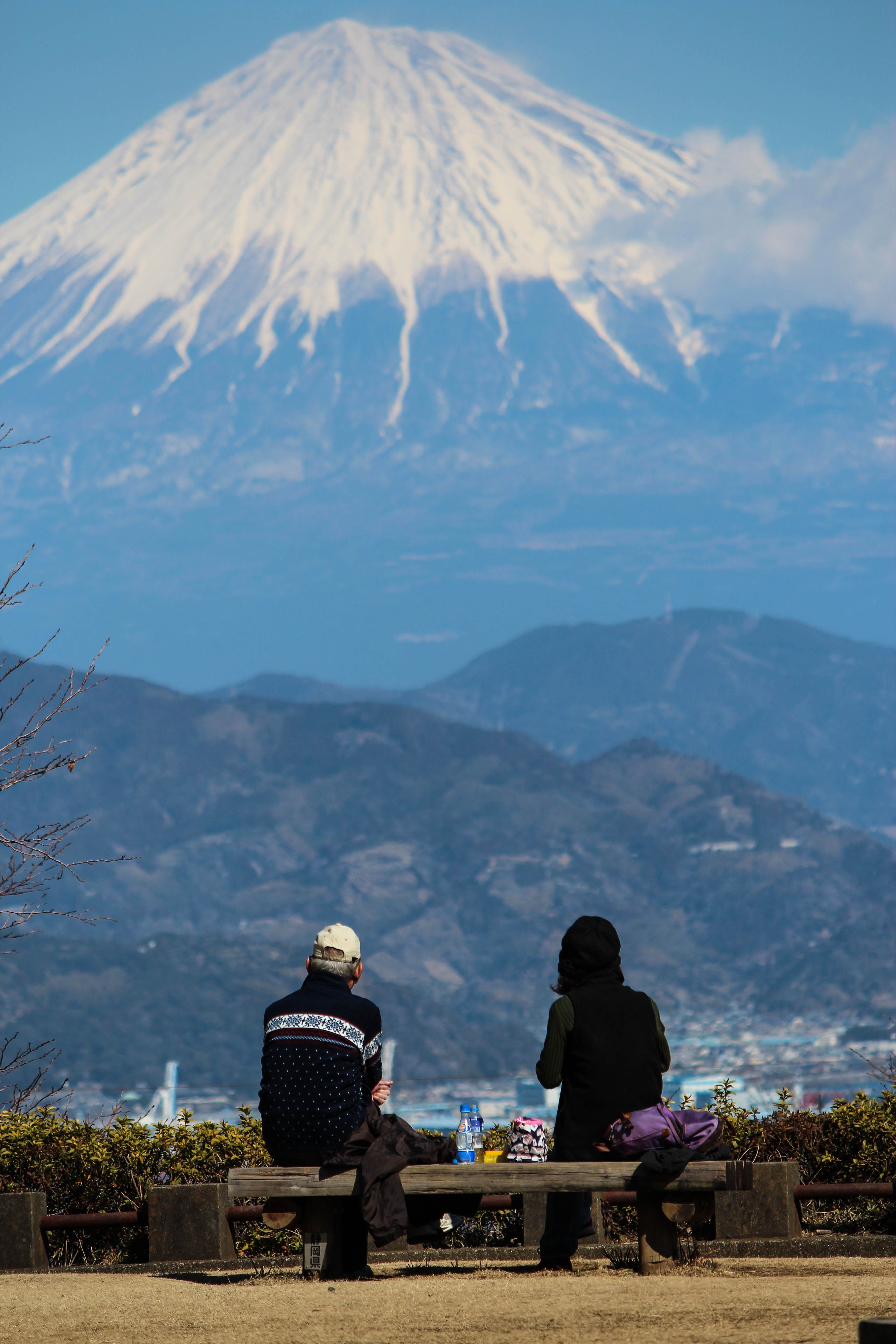 Two Japanese people share lunch on a park bench overlooking Mt Fuji. Captured February 2013 from Shizuoka.