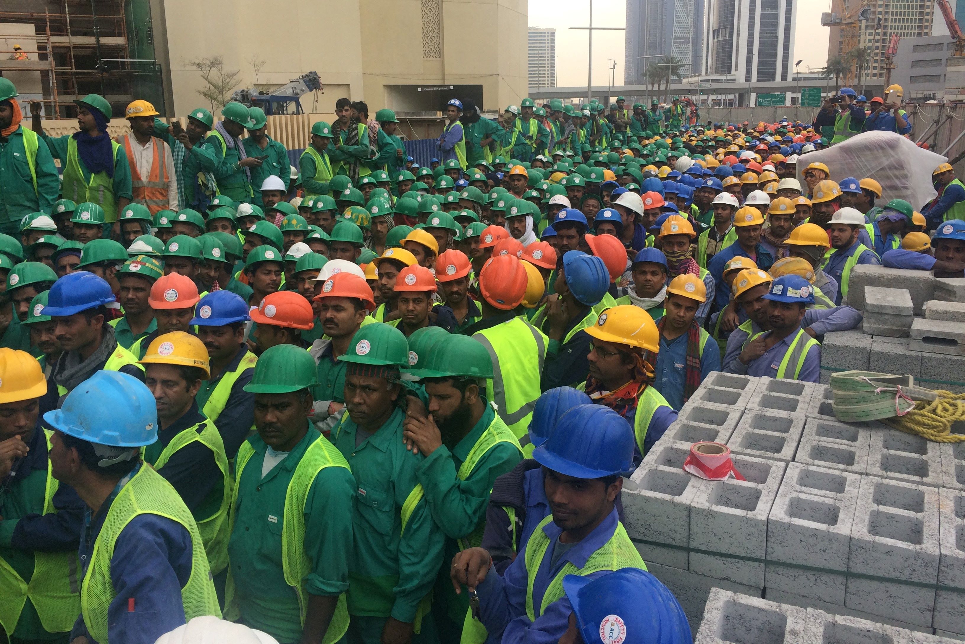Workers of all ethnicities stand together, ready to start the long day. Their helmets denote their roles on site.