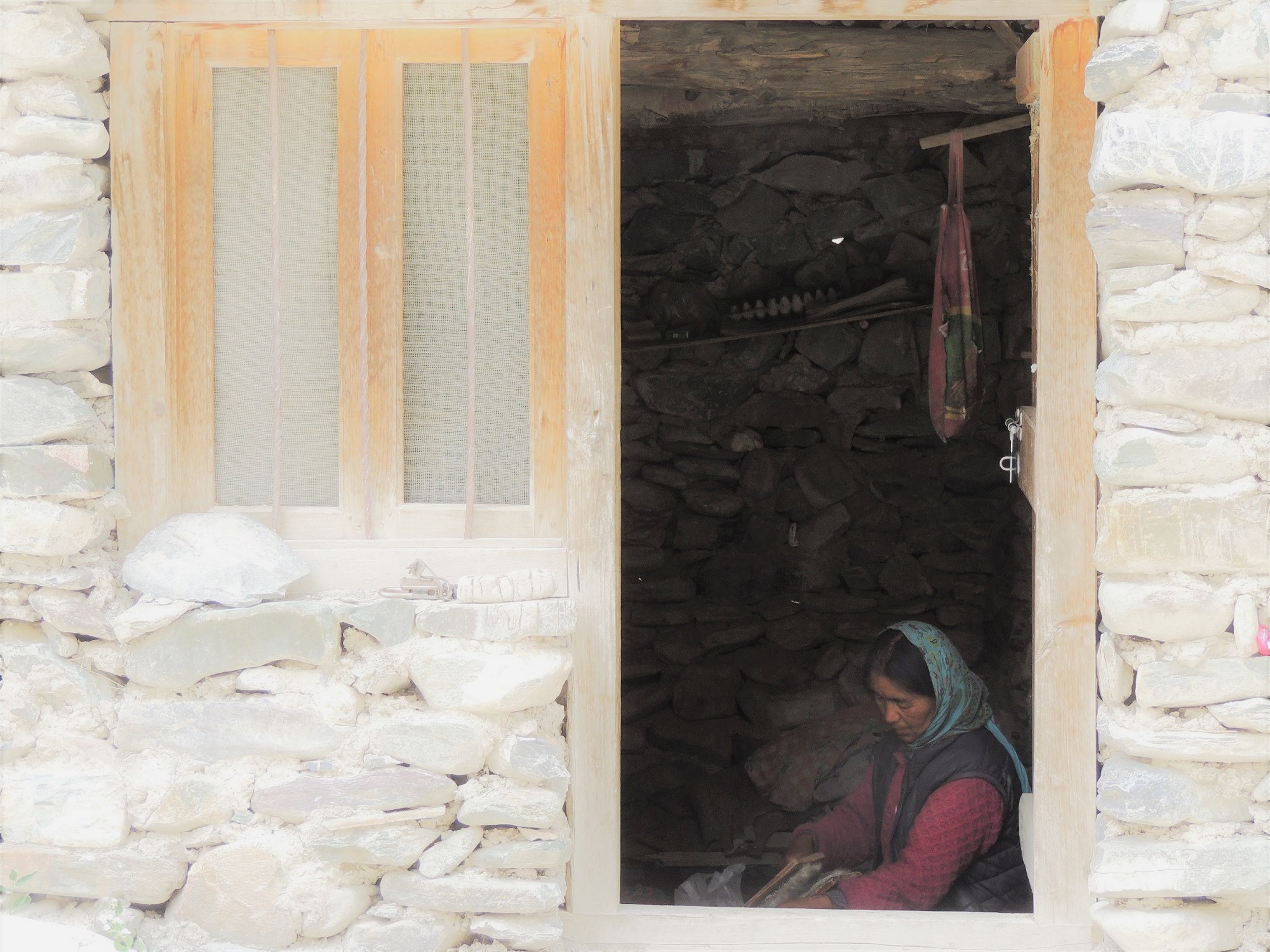 An elderly women is sitting on compressed soil in the entrance of her dark stone house, weaving wool by hand. It is not easy to get by in the small mountain village Skiu, situated 3500 metres above sea level, in the North Indian stone dessert.