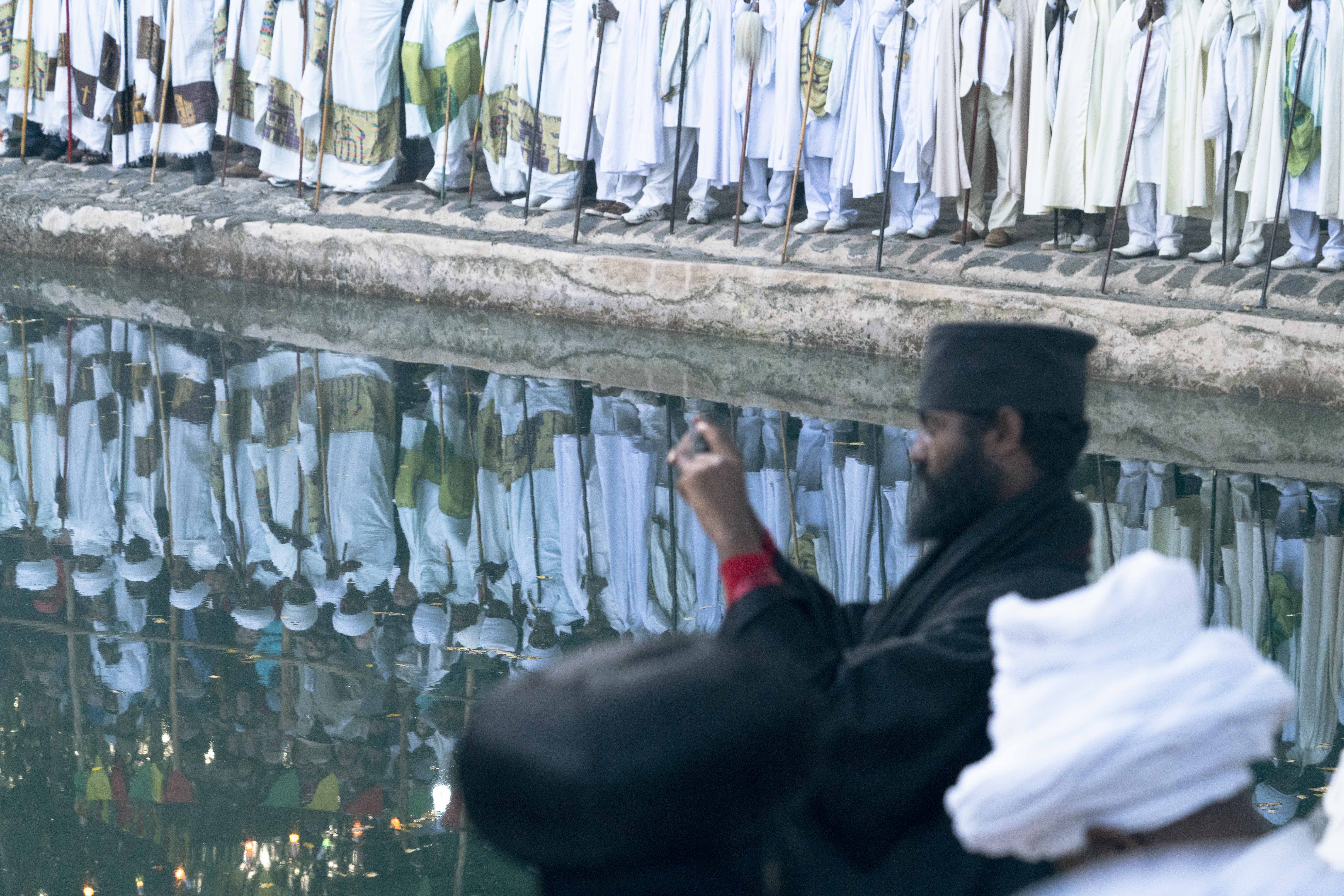 By the time the sun rises, thousands have gathered to hear the priests  but many must settle for a place outside the walls of the main church arena. The spectacle is not lost on this senior priest who documents the experience on his smartphone.