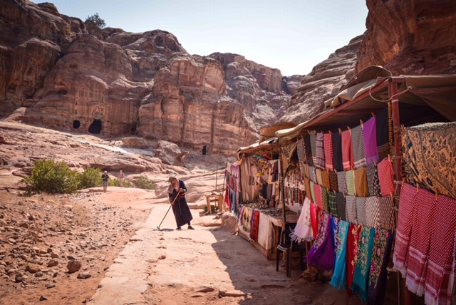 A Bedouin woman sweeps the trail in front of her shop as she awaits customers in Petra.