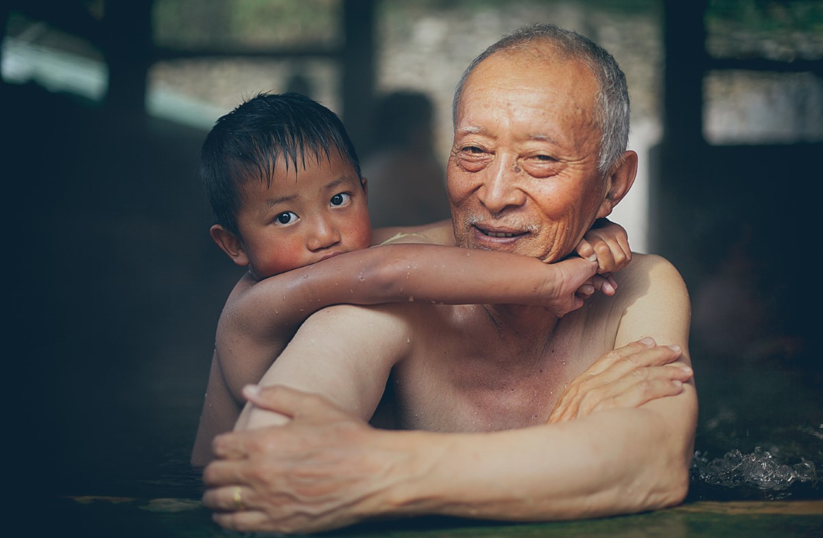 Far away in Gasa, Bhutan, an elderly man enjoys the holy hot springs with his grandson.