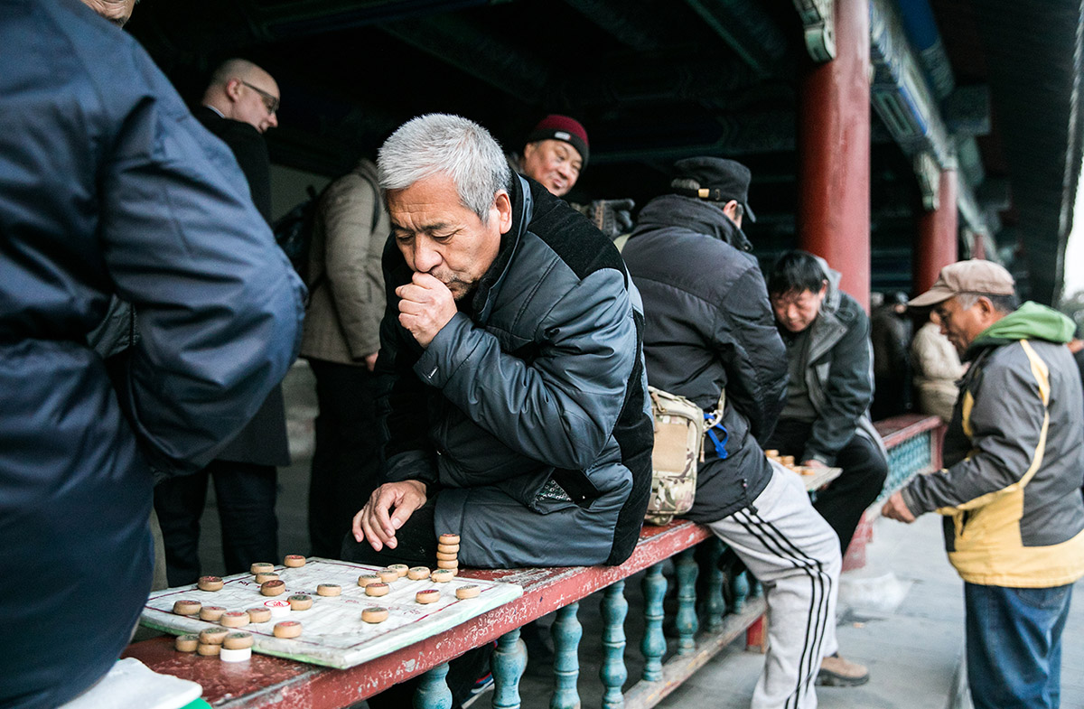 A man warms up his hands between plays. Even though it is only 45°F (7°C), people are still outside, enjoying the temple gardens, as well as each other's company.