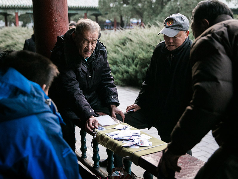 An elderly man lays down his cards to play as two young boys watch intently. Even with new technology, there is a sense of value in a more traditional way of spending leisure time, and it goes beyond generations.