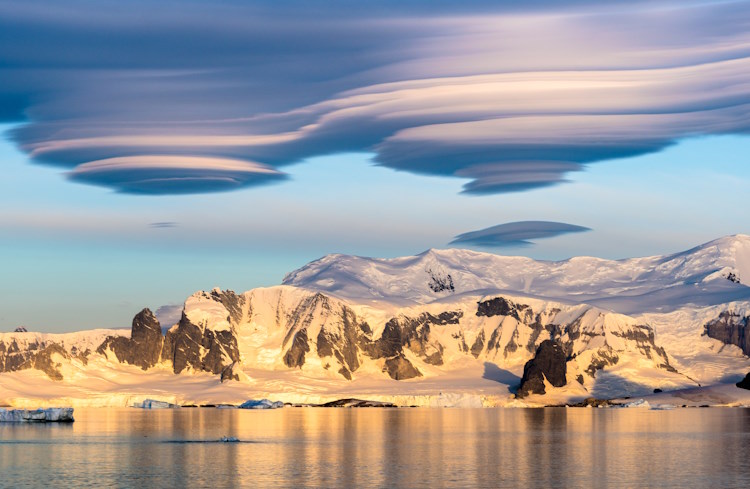 Dramatic clouds shaped like UFOs gather over mountain peaks in Antarctica.