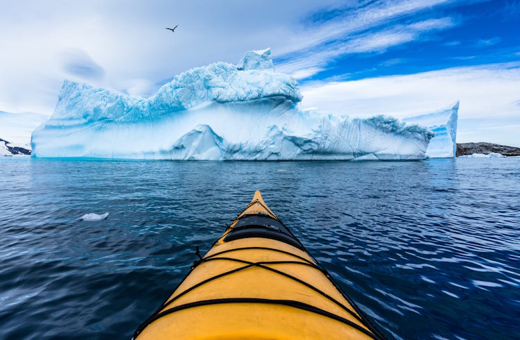 The nose of a kayak as it approaches a large iceberg in Antarctica.