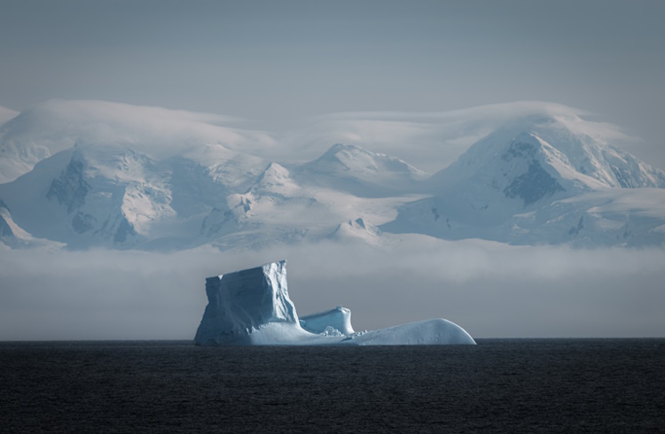 A massive iceberg is dwarfed by snow-covered mountains in Antarctica.