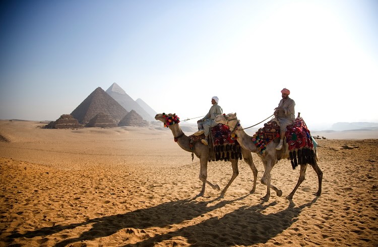 People riding camels in front of the pyramids
