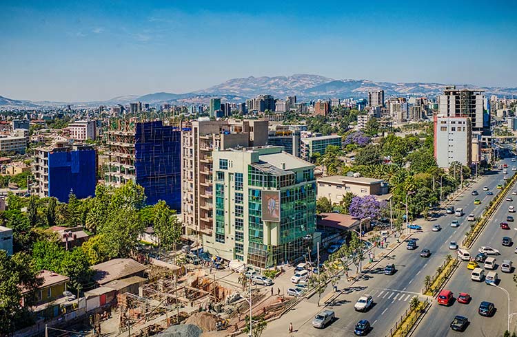 A panoramic view of a city from above, mountains in the distance and many cars on the streets