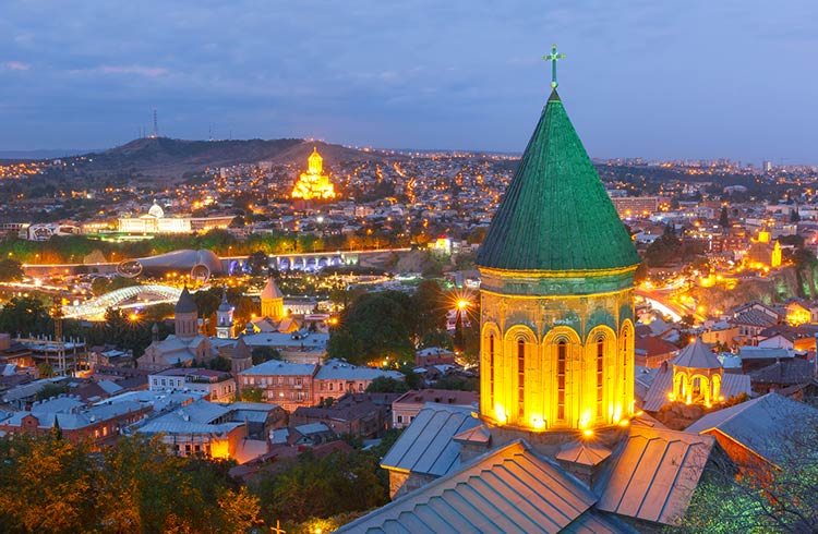 Aerial view of Old Town with dome of Lower Bethlemi Church and Sameba Holy Trinity Cathedral, Metekhi Church, bridge of Peace and Presidential Palace in night Illumination during evening blue hour, Tbilisi, Georgia