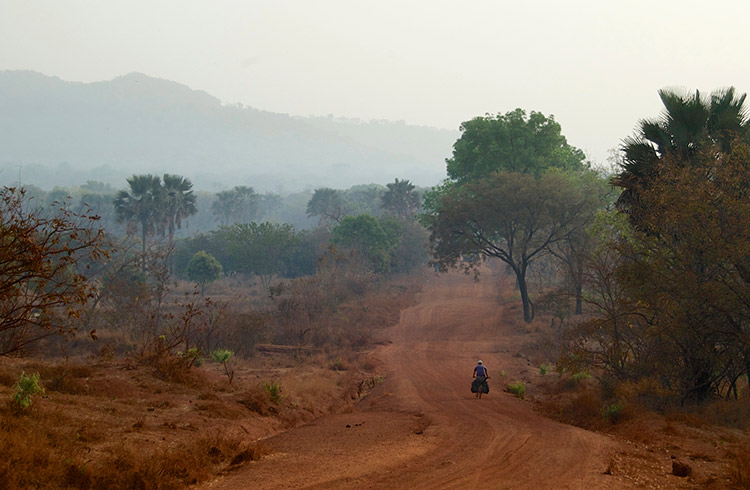 A man riding a bicycle along a dusty road in Guinea