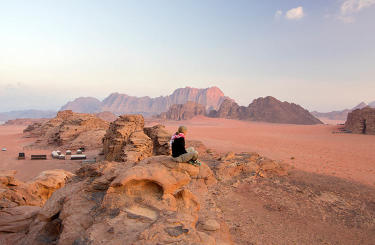 A woman sits on a rock in a deserted landscape in Jordan