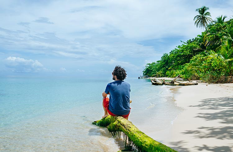 A man sitting on a tree trunk on Bocas del Toro, Cayo Zapatilla, Panama