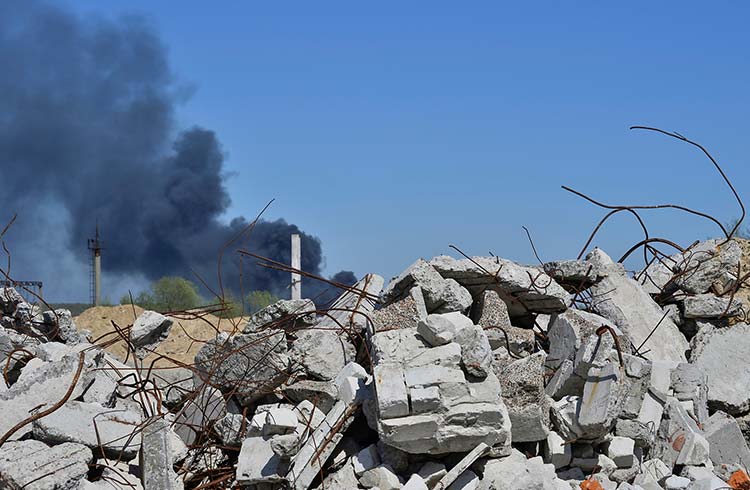 A pile of concrete rubble with protruding rebar on the background of thick black smoke in the blue sky