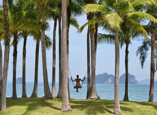 A woman on a swing between two palm trees on a picturesque Thailand beach