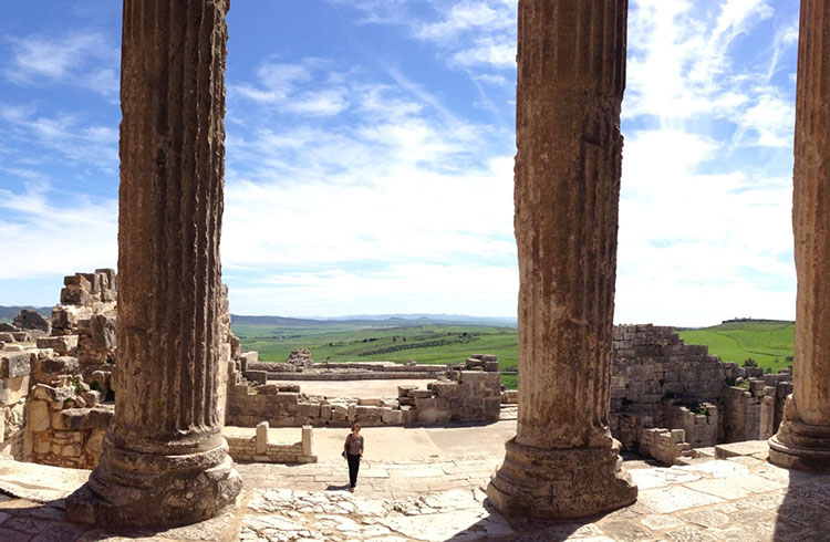A woman stands beneath the large columns at Dougga, Tunisia