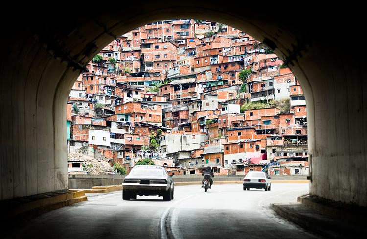 Two cars and a motorcycle pass through a tunnel on a street in Caracas, in the background you can see a skyline of buildings
