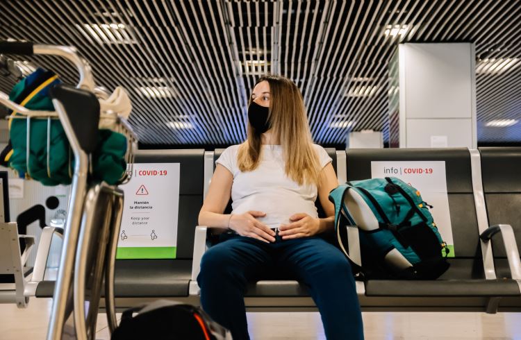 A pregnant woman sits in an airport boarding area wearing a face mask.