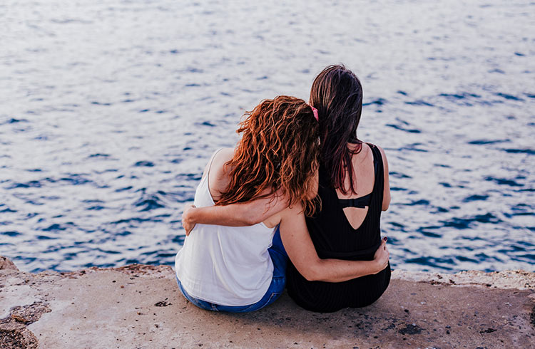 Lesbian Women With Arm Around Sitting At Beach