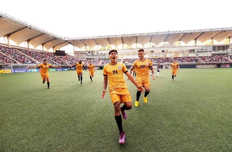 Ecstatic male soccer player runs down a stadium field cheering in celebration during an international match