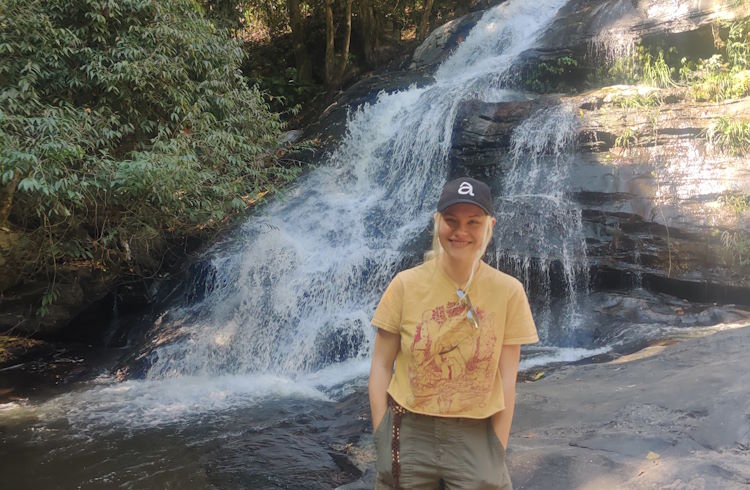 A solo female traveler stands in front of a waterfall in Thailand.