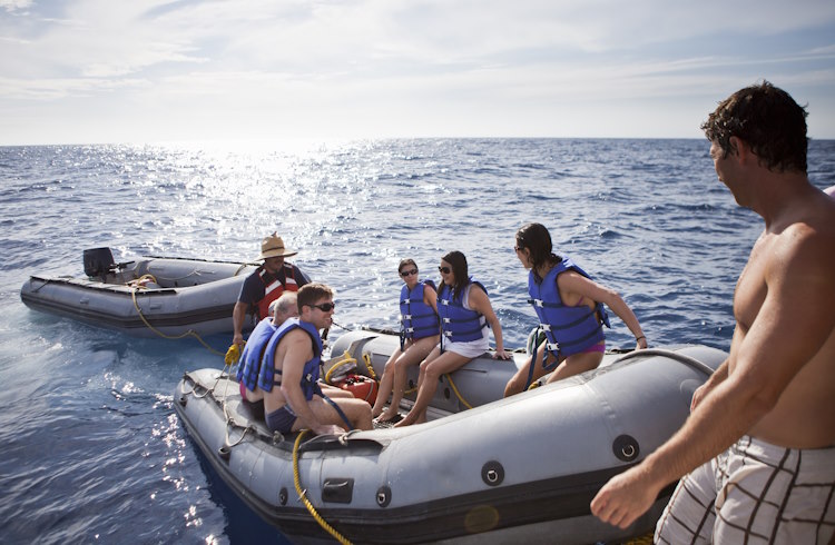 A dinghy full of passengers pulls up to a live-aboard boat.