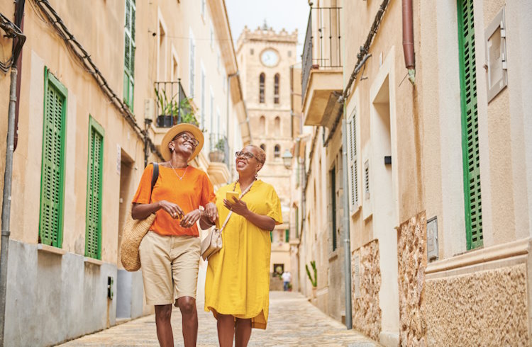 Two mature Black women walk down an historic street in Majorca, Spain. 