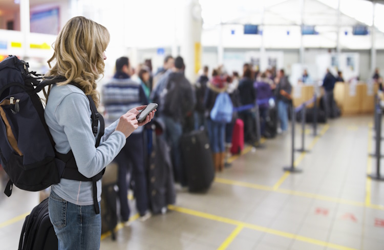 A woman checks her phone at an airport next to a long security line.