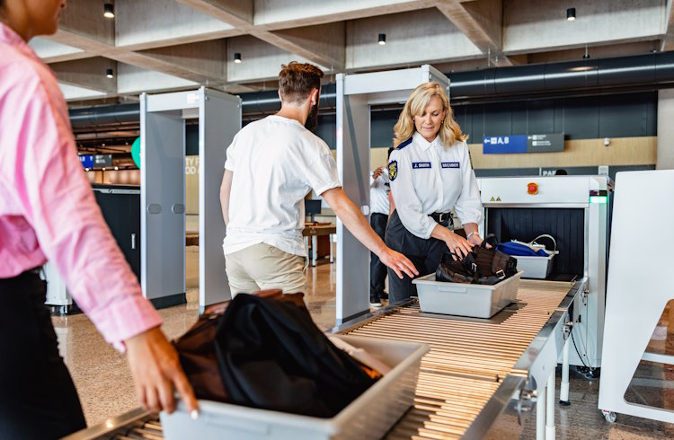 Travelers at an airport security check place their trays on the X-ray conveyor belt.