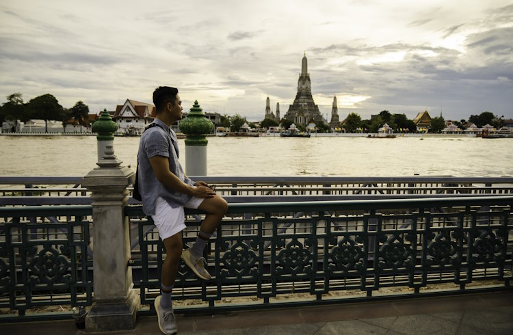 A male traveler gazes at the river in Bangkok at sunset.