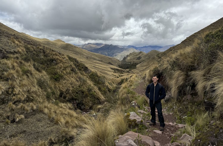 A traveler stands on a path leading to rugged mounain peaks. 