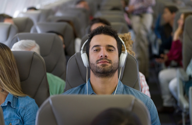A man wearing headphones relaxes on a flight.