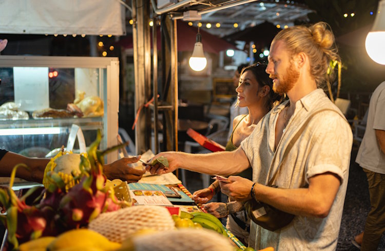 Two travelers pay cash for a meal at a night market in Thailand. 