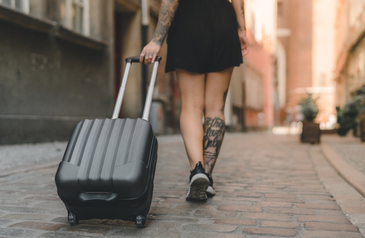 A woman with arm and leg tattoos pulls a rolling suitcase down a cobbled street in Poland.