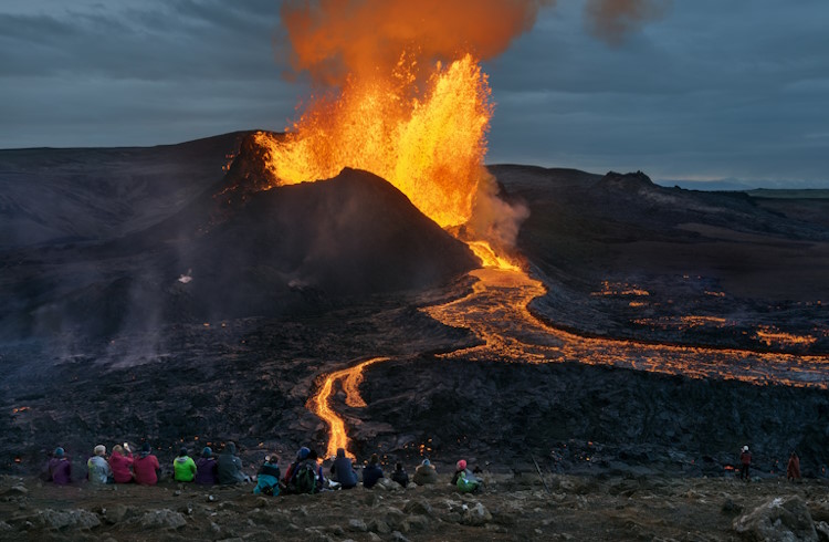 Tourists watch from a distance as iceland's Fagradalsfjall volcano sends molten lava into the air.