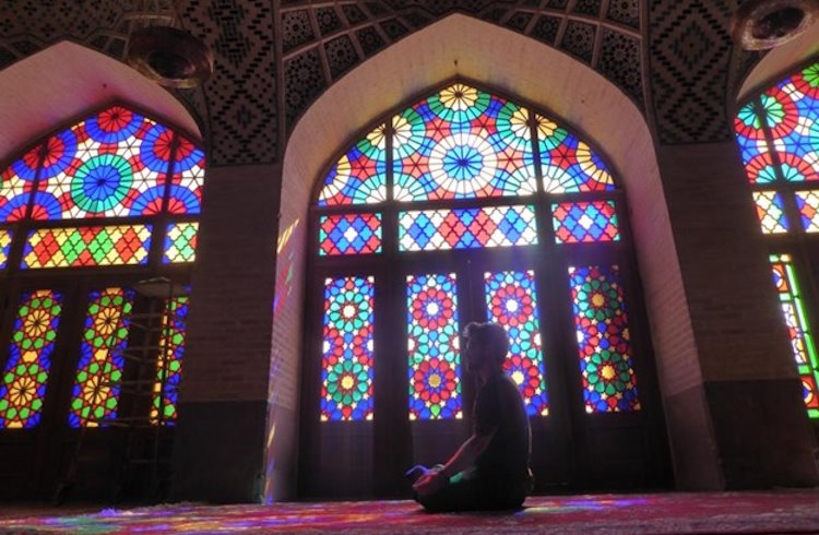A traveler kneels on the floor of a mosque in Iran.