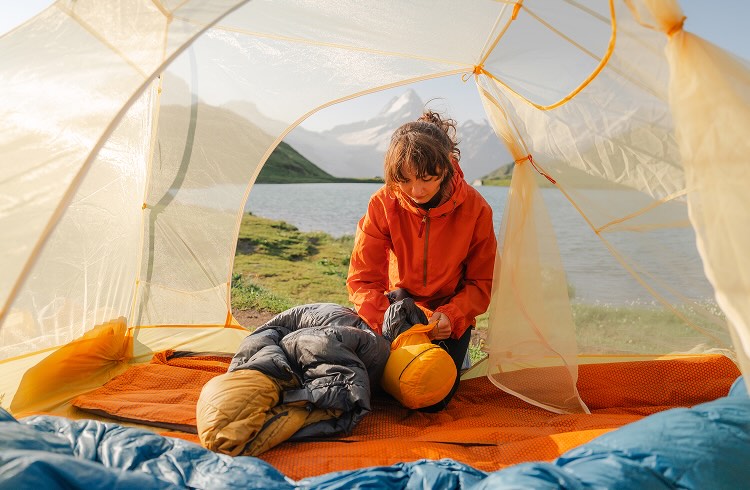 A woman kneeling in a tent packing away her sleeping bag