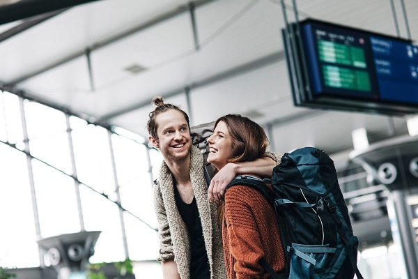 A smiling couple traveling together, wearing backpacks at the airport