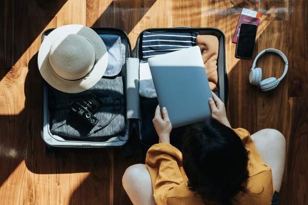 Overhead view of young Asian woman packing a suitcase for a trip at home. 